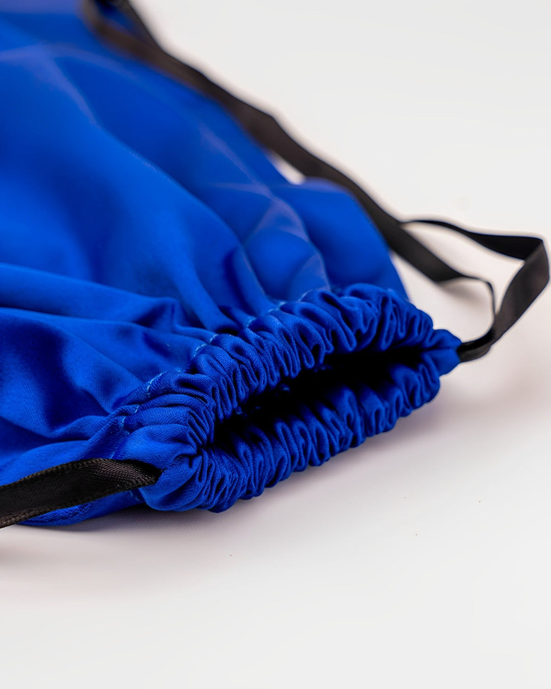 A close-up image of the 19 Momme Silk U-Shaped Pillow Travel Set by SusanSilk, showcasing the shiny blue silk fabric and gathered top edge with black drawstrings.