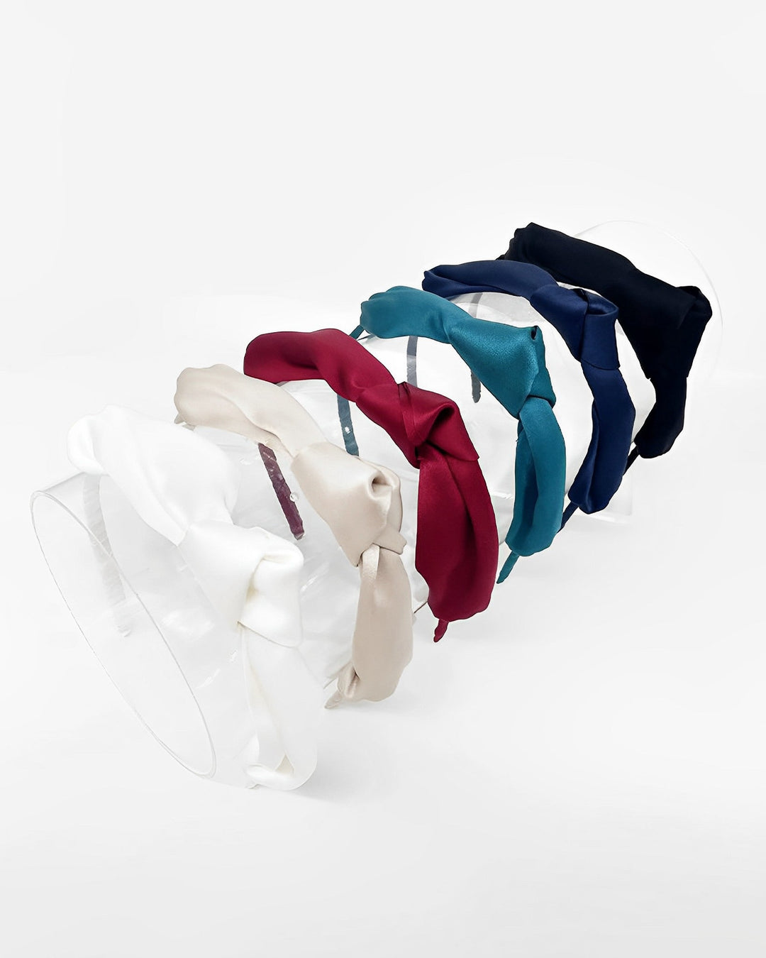 A set of six colorful Pure Color Bow Knot Silk Headbands by SusanSilk, featuring white, beige, red, teal, navy blue, and black bow designs arranged in a row and elegantly displayed against a white background.