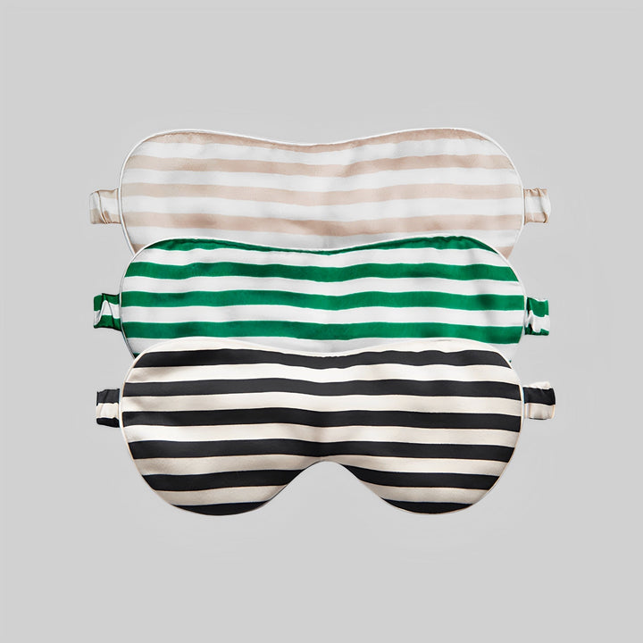 Three 19 Momme Stripe Silk Sleep Eye Masks from SusanSilk are stacked on a light grey background. The masks are arranged with beige and white on top, green and white in the middle, and black and white at the bottom.