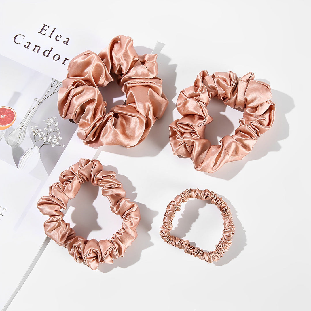 Four pink satin scrunchies from the 22 Momme Luxury Silk Scrunchies Set 4-Pack by SusanSilk are placed next to a magazine on a white surface, showcasing the elegance of SusanSilk designs.