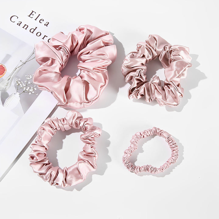 Four 22 Momme Luxury Silk Scrunchies from the SusanSilk 4-Pack set, each in pink and differing in size, are elegantly displayed on a white surface alongside a magazine page.