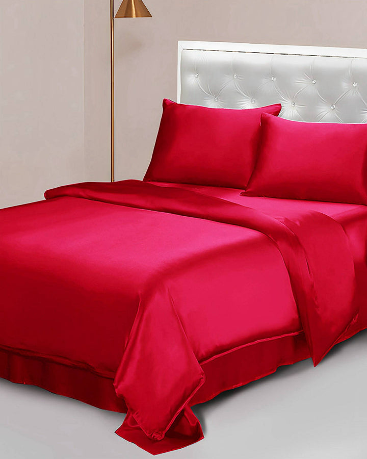 A neatly made bed with the SusanSilk 25 Momme Seamless Luxury Duvet Cover in bright red and matching pillowcases is placed against a light-colored wall with a tufted headboard. A slim, gold floor lamp stands next to the bed.