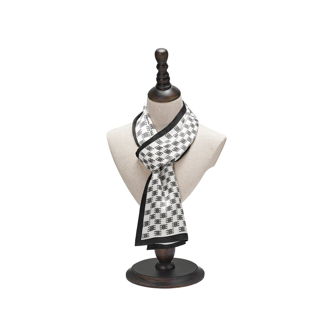 The SusanSilk Arc De Triomphe Narrow Long Silk Scarf, featuring a black and white pattern, is draped over a beige mannequin bust on a wooden stand.