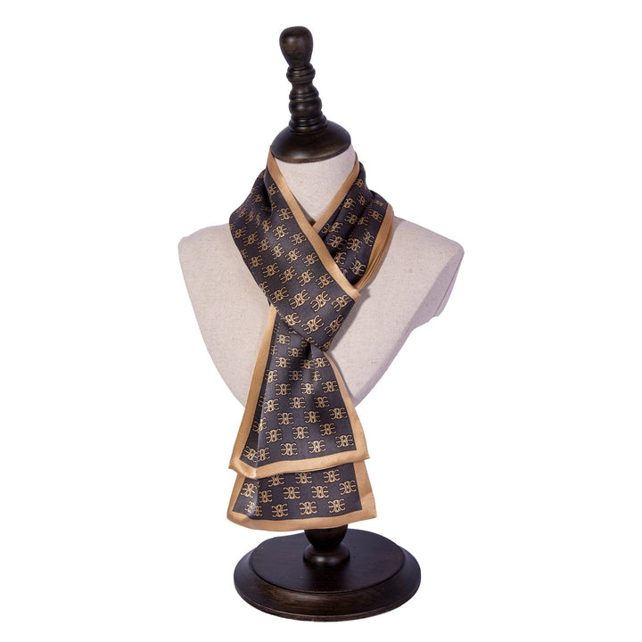 Mannequin displaying the Arc De Triomphe Narrow Long Silk Scarf from SusanSilk, featuring a dark silk base with a repeating gold pattern and bordered by a lighter gold trim. The mannequin stands on a wooden base.