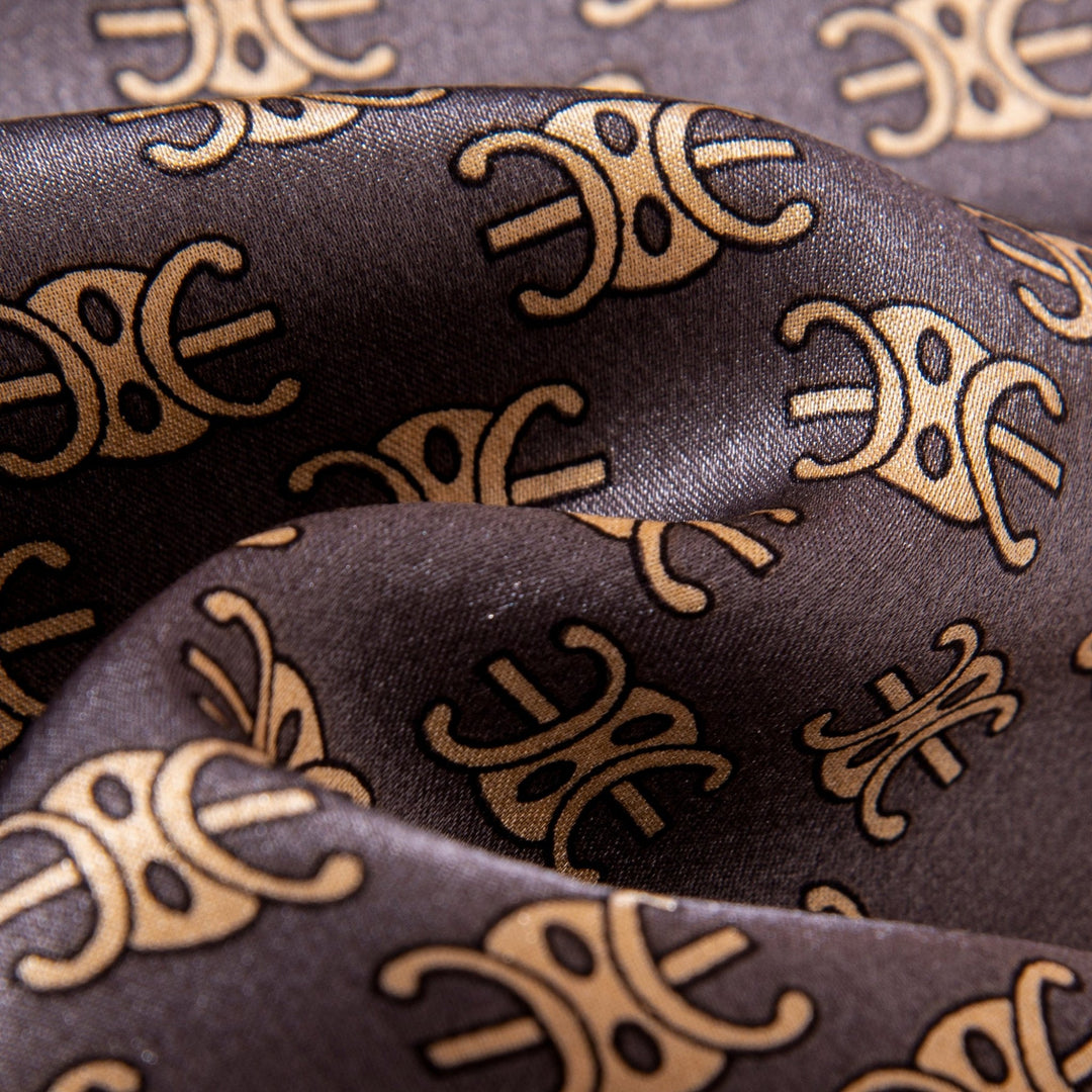 Close-up of the Arc De Triomphe Narrow Long Silk Scarf by SusanSilk, featuring a gold, symmetrical pattern on a dark brown background. The smooth folds and silky texture underscore its luxurious feel.