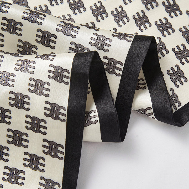 A detailed view of the Arc De Triomphe Narrow Long Silk Scarf from SusanSilk showcases its luxurious fabric adorned with a black and white pattern featuring symmetrical motifs, complemented by black borders along the edges.