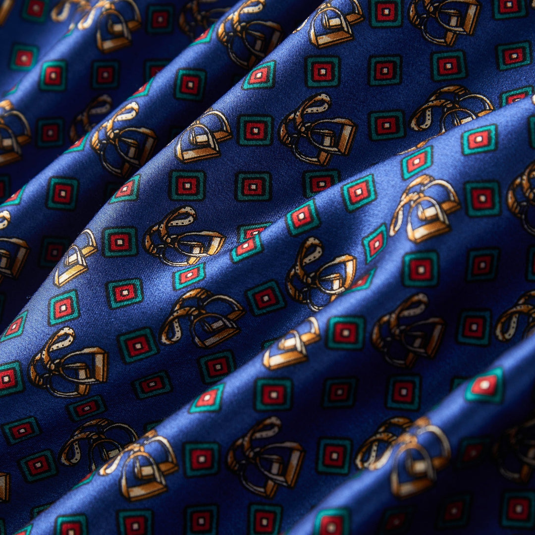 A close-up of the Buckle Pattern Long Silk Brushed Scarf by SusanSilk, showcasing a blue fabric adorned with an intricate design of green and red squares interwoven with yellow, gold, and brown interlocking chains.