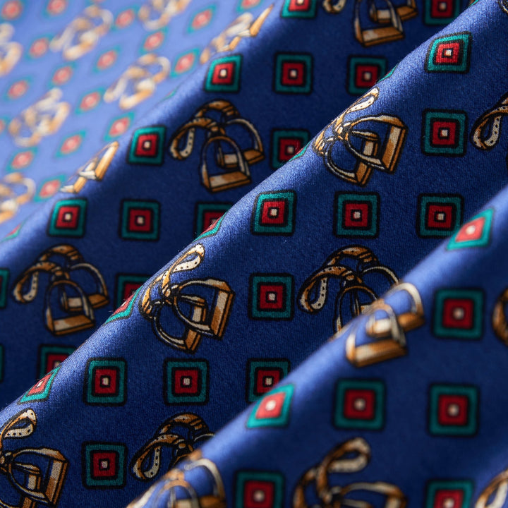 Close-up of SusanSilk's Buckle Pattern Long Silk Brushed Scarf, showcasing an ornate blue silk fabric adorned with alternating red and green squares and intricate golden ribbon motifs.