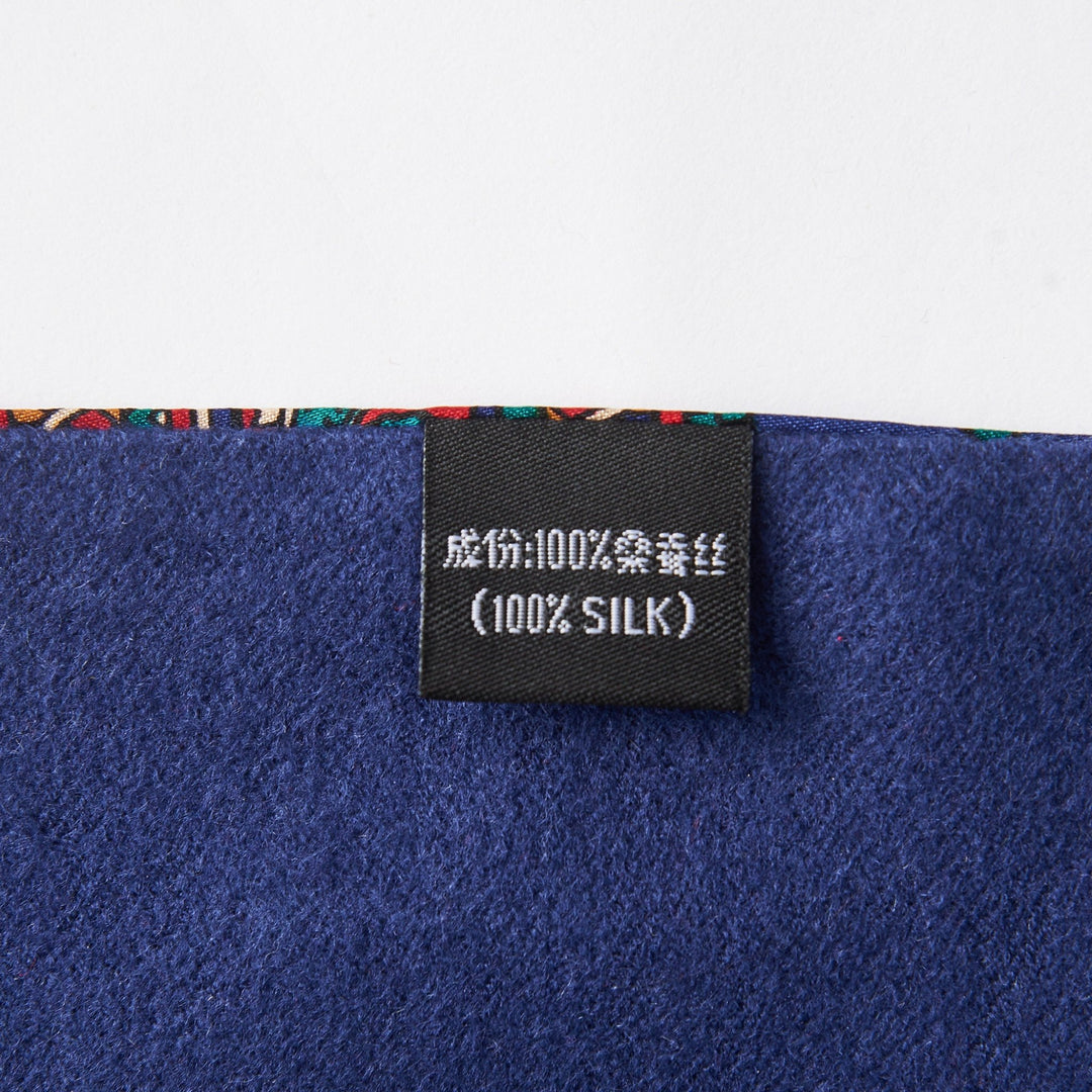 Close-up of a fabric tag displaying "100% Silk" in both Chinese characters and English, attached to a Buckle Pattern Long Silk Brushed Scarf by SusanSilk, featuring rich dark blue material and a vibrant edge.