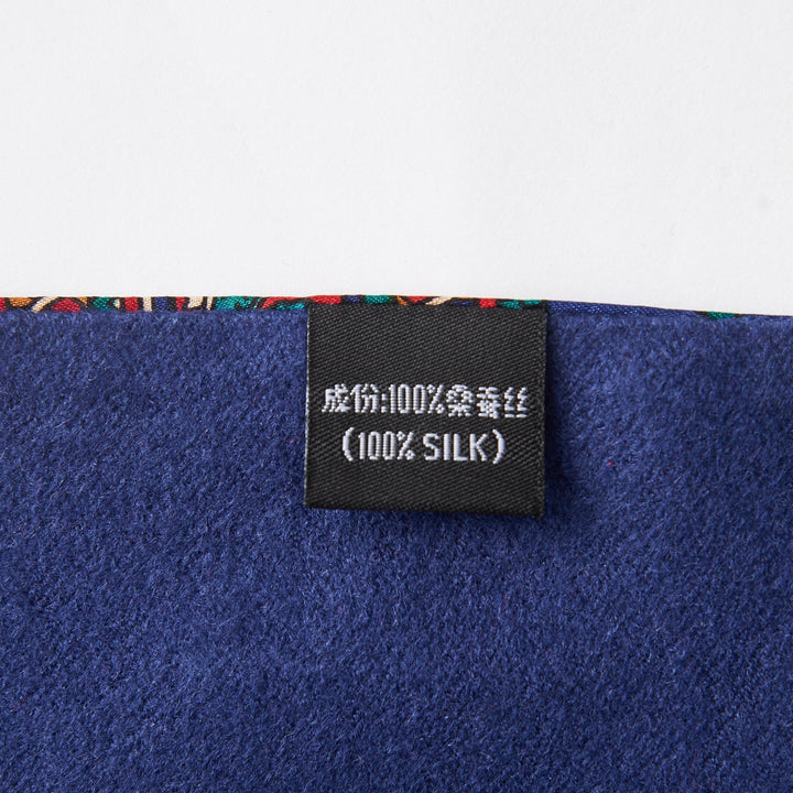 Close-up of a fabric tag displaying "100% Silk" in both Chinese characters and English, attached to a Buckle Pattern Long Silk Brushed Scarf by SusanSilk, featuring rich dark blue material and a vibrant edge.