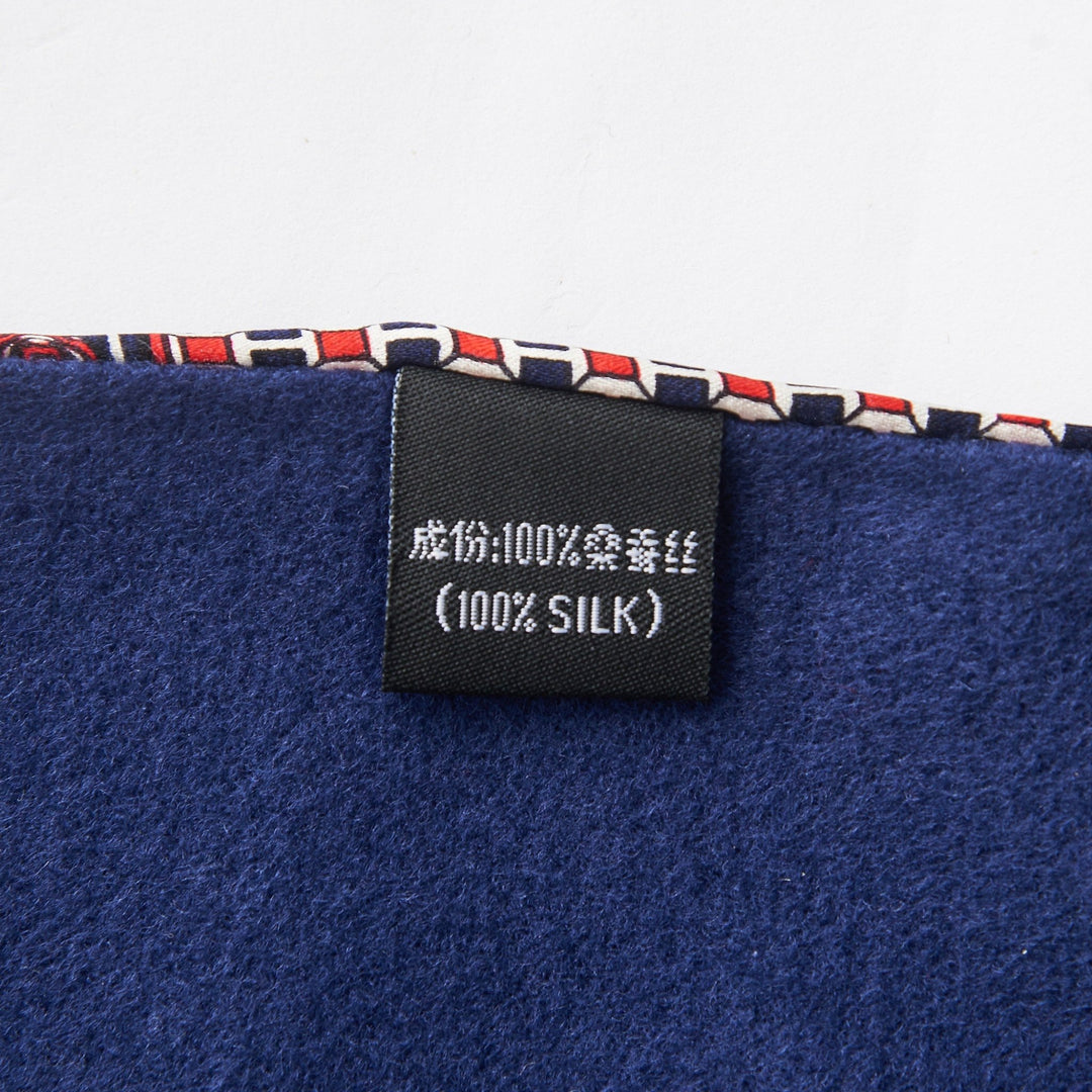 Close-up image of a black fabric tag labeled "100% SILK" sewn onto a blue textile with a patterned trim from the renowned SusanSilk Cross Pattern Long Silk Brushed Scarf.