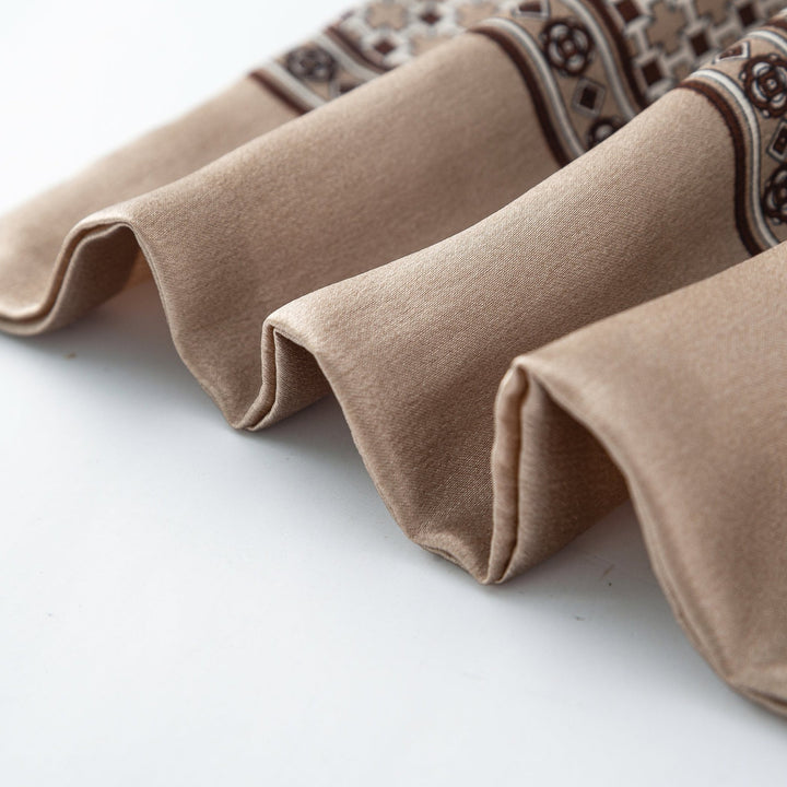 Close-up of the edge of a beige silk fabric with a decorative brown and white pattern, showing neatly folded layers of the Cross Pattern Long Silk Scarf by SusanSilk.