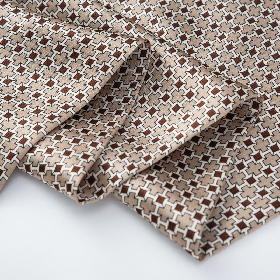 A close-up of a folded Cross Pattern Long Silk Scarf by SusanSilk, showcasing its beige, white, and brown cross design.