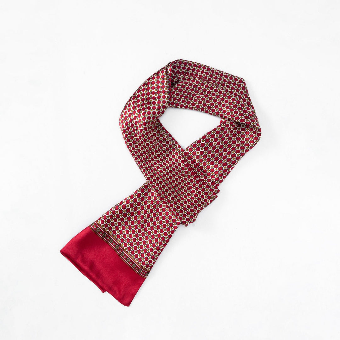 A Cross Pattern Long Silk Scarf by SusanSilk, featuring a red hue with a geometric pattern of small hexagons and a solid red border, is neatly laid out on a white surface.