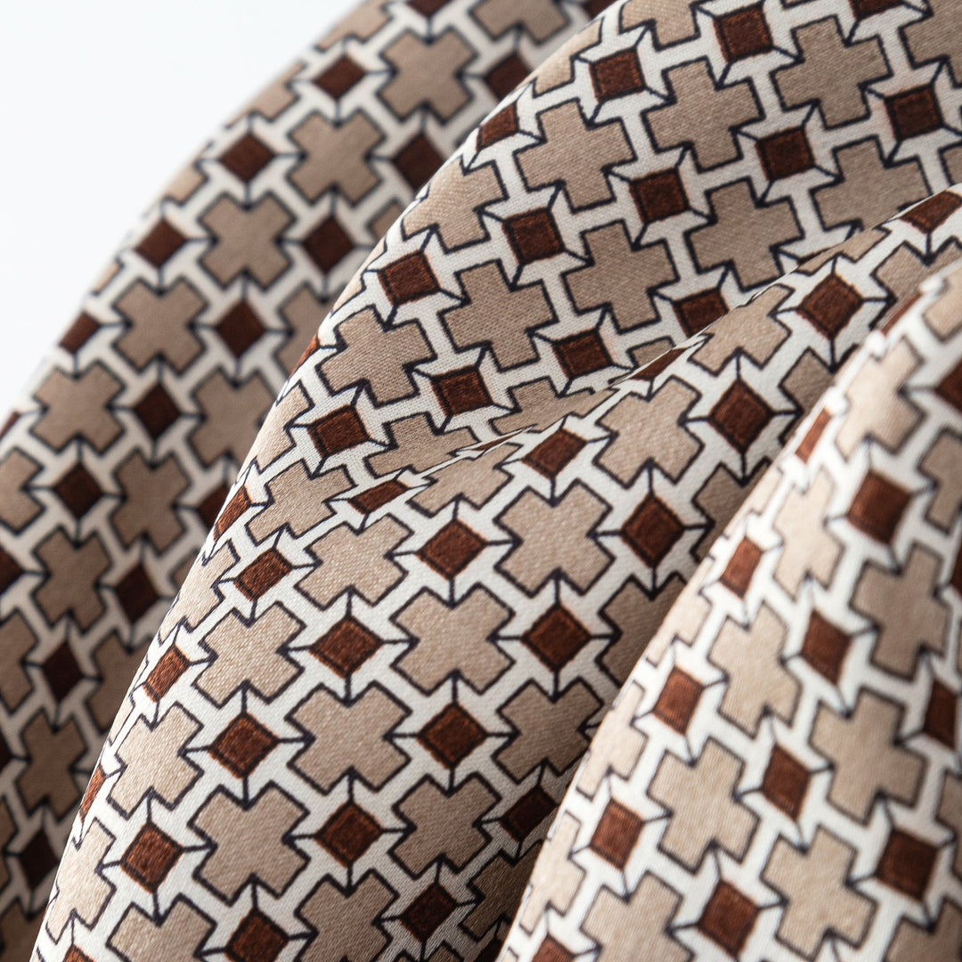 Close-up of the SusanSilk Cross Pattern Long Silk Scarf, showcasing its geometric design with beige and brown cross shapes bordered by dark lines. The image captures three folds of the fabric.