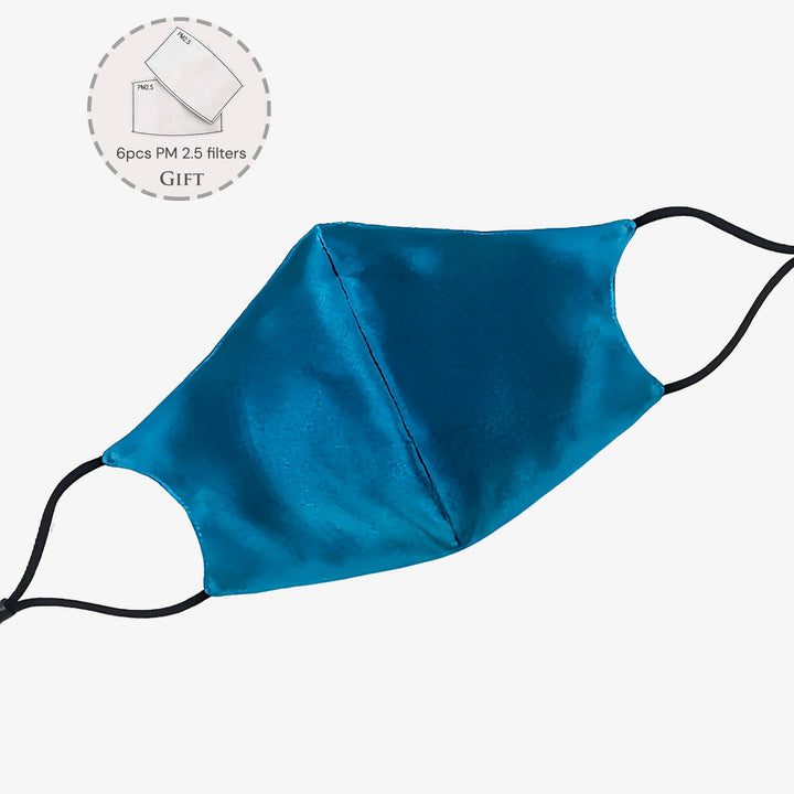 This SusanSilk Double Layer Silk Face Mask with Nose Wire (set of 3) features a blue design with black ear loops, crafted from soft susansilk for utmost comfort. The product also includes an inset image displaying the gift of 6 PM 2.5 filters.