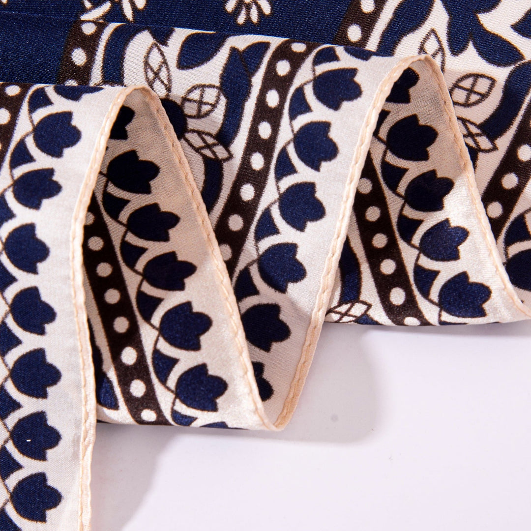 A close-up shot of a Floral Pattern Square Silk Scarf by SusanSilk, showcasing its intricate design with blue, black, and white motifs. The scarf features a mix of stripes, leaves, and dots and is elegantly folded in a wavy shape.