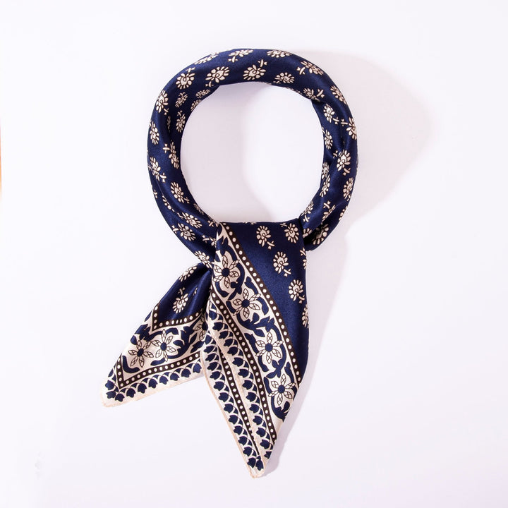 A Floral Pattern Square Silk Scarf by SusanSilk, adorned with navy blue, white floral, and geometric designs, neatly tied in a loop against a white background.