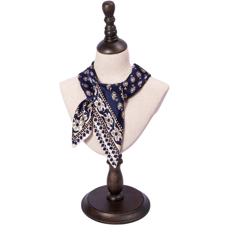 A mannequin bust displays a SusanSilk Floral Pattern Square Silk Scarf in navy blue, adorned with white designs and tied in a knot.