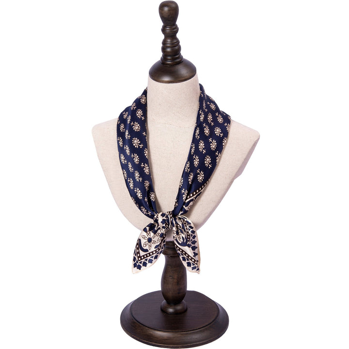 A Floral Pattern Square Silk Scarf by SusanSilk, featuring navy blue and white tones, is elegantly displayed on a beige mannequin bust that is mounted on a dark wooden stand.