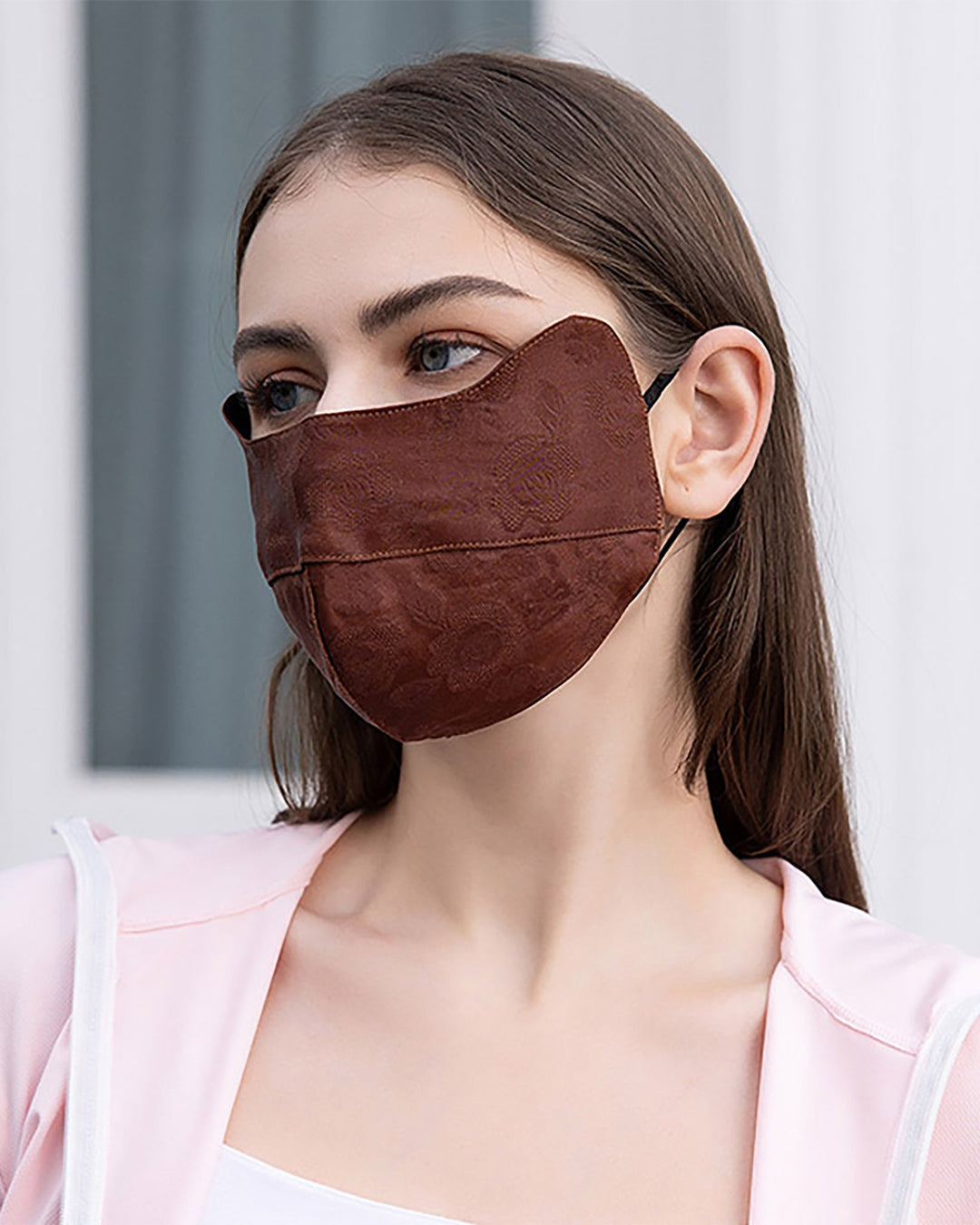 A woman with long brown hair wears a SusanSilk Jacquard Upturned Brim Hat & Face Mask and a light pink hoodie, standing in front of a blurred background.