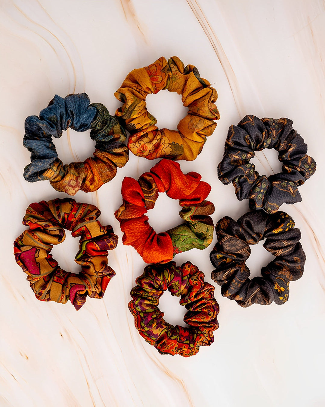 Seven Gambiered Canton Gauze Silk Scrunchies by SusanSilk, each 3cm wide, are arranged in a circle on a light background, showcasing various colors and patterns including blue, yellow, red, and multicolored designs.