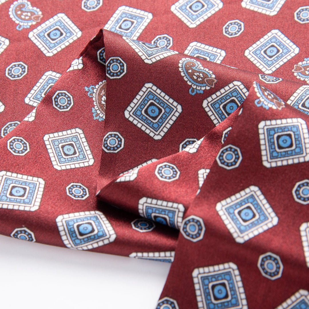 A close-up of the Gemstone Long Silk Scarf by SusanSilk, showcasing its burgundy fabric adorned with a blue and white geometric and paisley pattern.