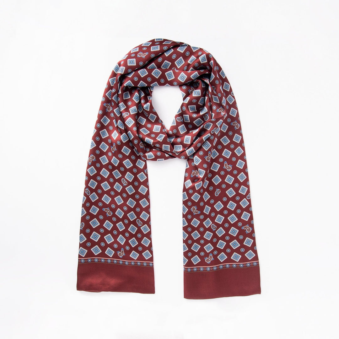 A maroon Gemstone Long Silk Scarf by SusanSilk, featuring small blue and white geometric patterns, folded in a loop on a white background.