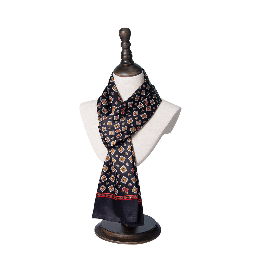 The Gemstone Long Silk Scarf by SusanSilk, featuring a blue geometric pattern and a striking red border, is elegantly displayed on a mannequin bust with a dark wood stand.