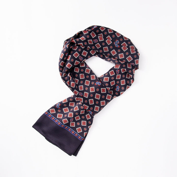 A folded SusanSilk Gemstone Long Silk Scarf featuring a geometric red, white, and blue pattern on a dark background.