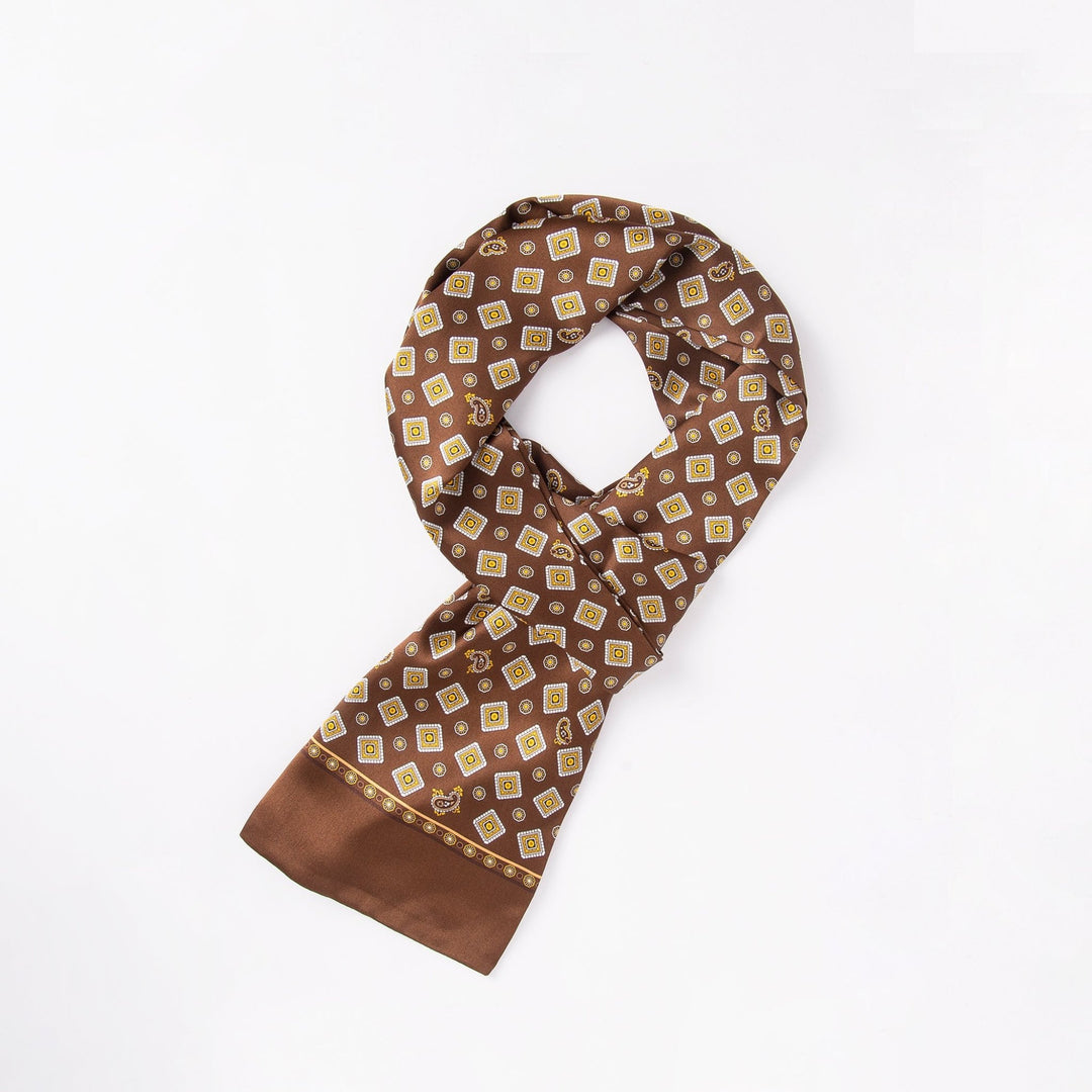 A SusanSilk Gemstone Long Silk Scarf, featuring a pattern of small yellow and white squares on a brown background, is neatly folded and laid on a white surface.