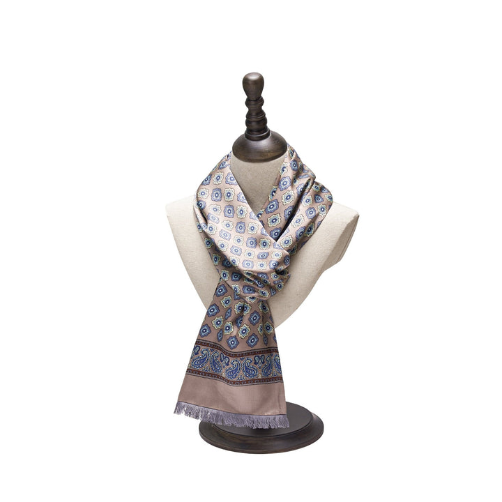 A mannequin displays the Geometric Pattern Long Silk Brushed Scarf in Ash-Gold from SusanSilk, featuring intricate blue and beige designs, draped elegantly around its neck.