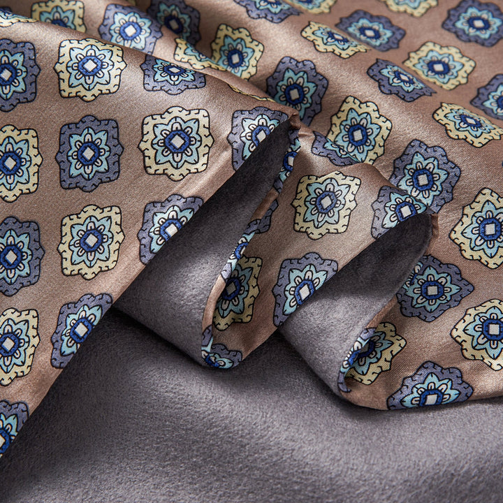 Close-up of the Geometric Pattern Long Silk Brushed Scarf - Ash-Gold from SusanSilk, showcasing its intricate geometric designs in blue, yellow, and brown tones draped over a solid grey background.