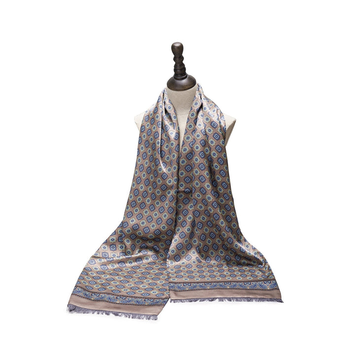 The Geometric Pattern Long Silk Brushed Scarf in Ash-Gold by SusanSilk is displayed on a mannequin bust, showcasing an intricate geometric design in blue and beige tones, perfectly embodying the elegance of SusanSilk craftsmanship.