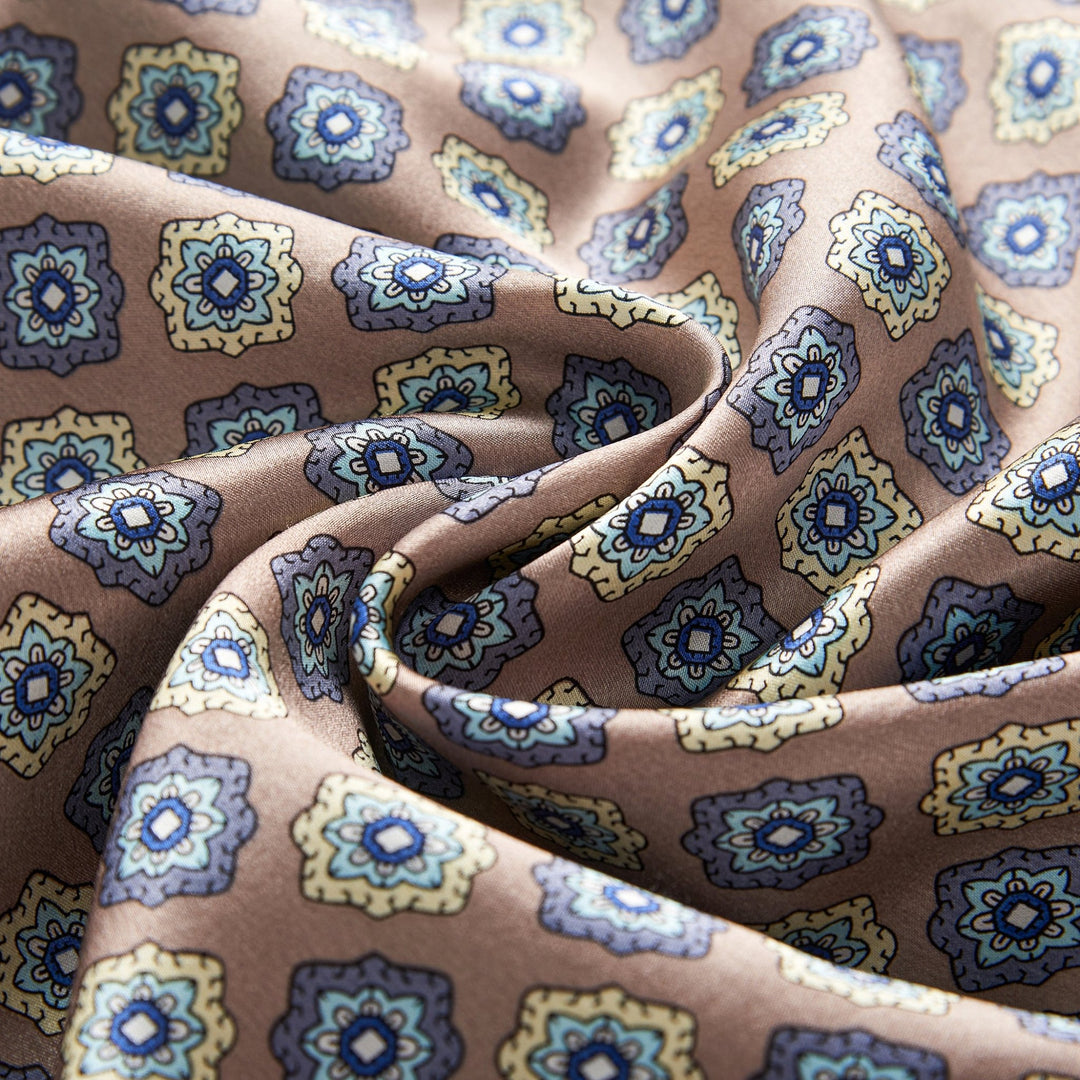 Close-up of the Geometric Pattern Long Silk Brushed Scarf - Ash-Gold by SusanSilk, showcasing a blend of blue and yellow floral motifs on a light brown background.