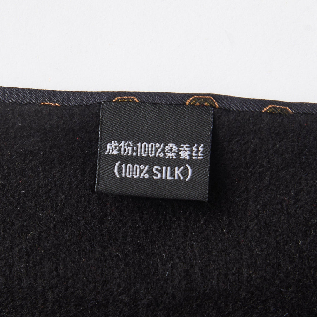 Close-up of the SusanSilk label on the Geometric Pattern Long Silk Brushed Scarf - Black, showing the fabric composition in Chinese and English, indicating that the material is "100% Silk." The label is attached to a dark-colored fabric.