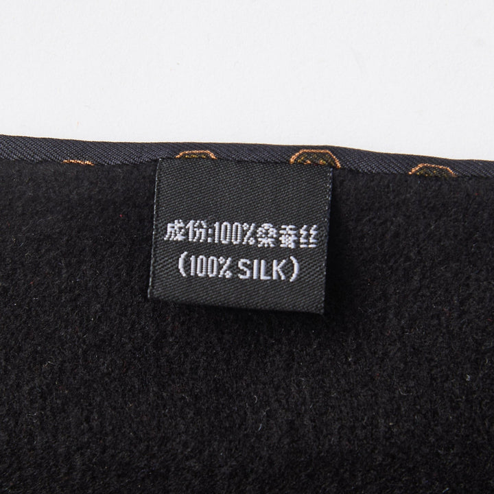 Close-up of the SusanSilk label on the Geometric Pattern Long Silk Brushed Scarf - Black, showing the fabric composition in Chinese and English, indicating that the material is "100% Silk." The label is attached to a dark-colored fabric.