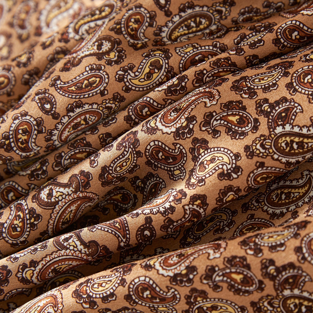 Close-up of the SusanSilk Paisley Long Silk Brushed Scarf - Gold, showcasing a detailed paisley pattern in intricate shades of beige and dark brown. The gold silk scarf is draped to highlight the luxurious texture and exquisite print.