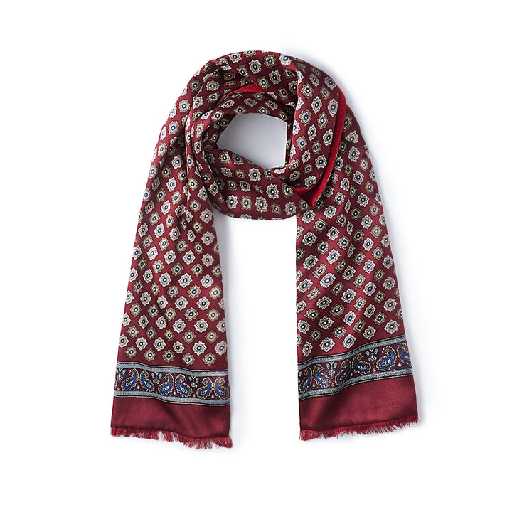 A luxurious SusanSilk Geometric Pattern Long Silk Brushed Scarf in red, featuring small white floral designs and a blue and red paisley border, is laid flat against a white background.