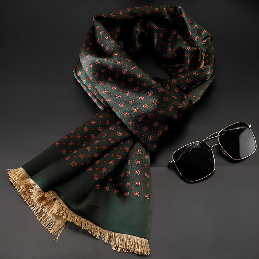 A SusanSilk Geometric Series Long Silk Brushed Scarf in green with a red polka dot pattern and tasseled ends is displayed next to a pair of black aviator sunglasses on a black surface.