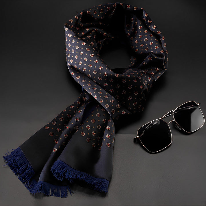 A SusanSilk Geometric Series Long Silk Brushed Scarf featuring a black pattern with red and white circles and blue fringes is displayed next to a pair of aviator sunglasses with black lenses and a wireframe.