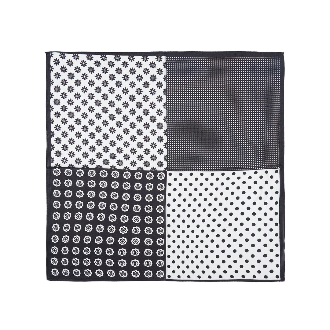 The Jigsaw Series Square Silk Scarf from SusanSilk showcases four distinct black and white patterns: small floral, dotted grid, circular floral, and polka dots, each occupying a quarter of the luxurious silk fabric.