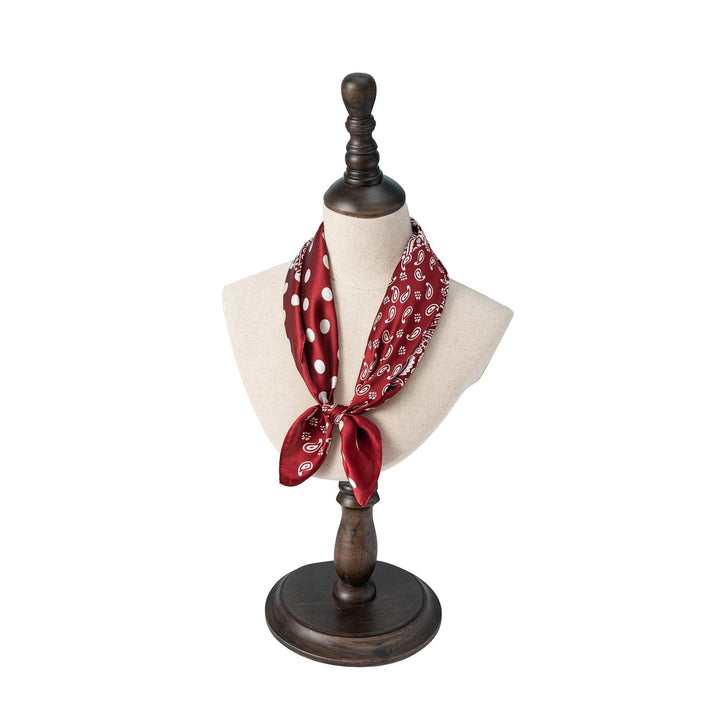 A red Jigsaw Series Square Silk Scarf from SusanSilk, featuring white paisley and polka dot patterns, tied around a beige mannequin bust on a dark wooden stand.