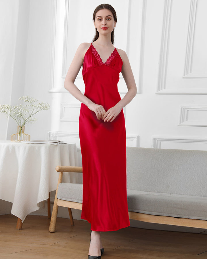 A woman in a red, sleeveless, V-neck Lace Long Silk Nightdress by SusanSilk is standing indoors. The room has white walls, a table with a vase of flowers, and a beige bench.