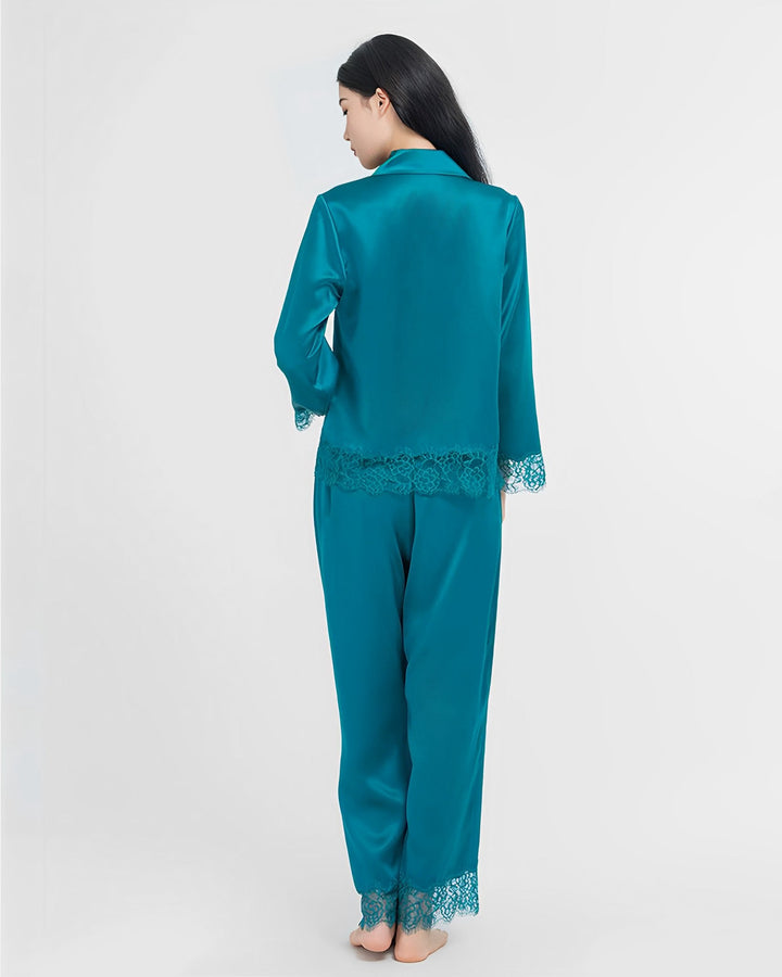 A woman with long dark hair stands with her back to the camera, wearing a teal Premium Lace Silk Pajamas Set from the SusanSilk collection, featuring delicate lace trim on the cuffs and hem.