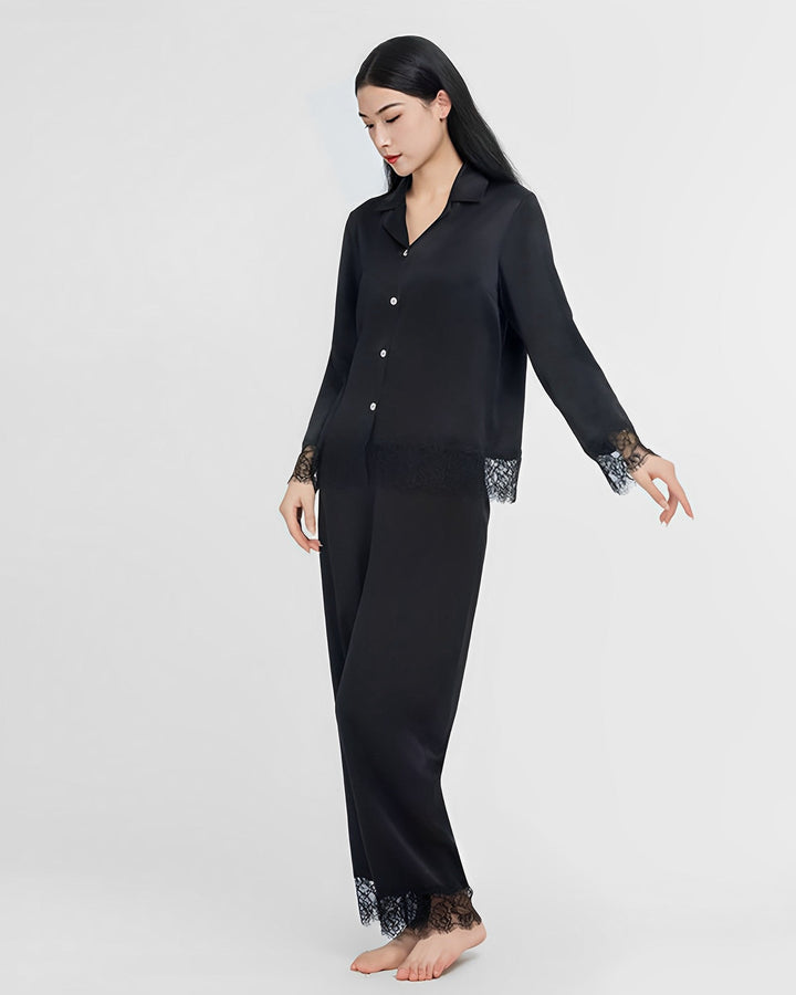 A woman stands posed against a plain background, wearing the Premium Lace Silk Pajamas Set by SusanSilk, which features matching black silk with lace detailing on the cuffs and hem.