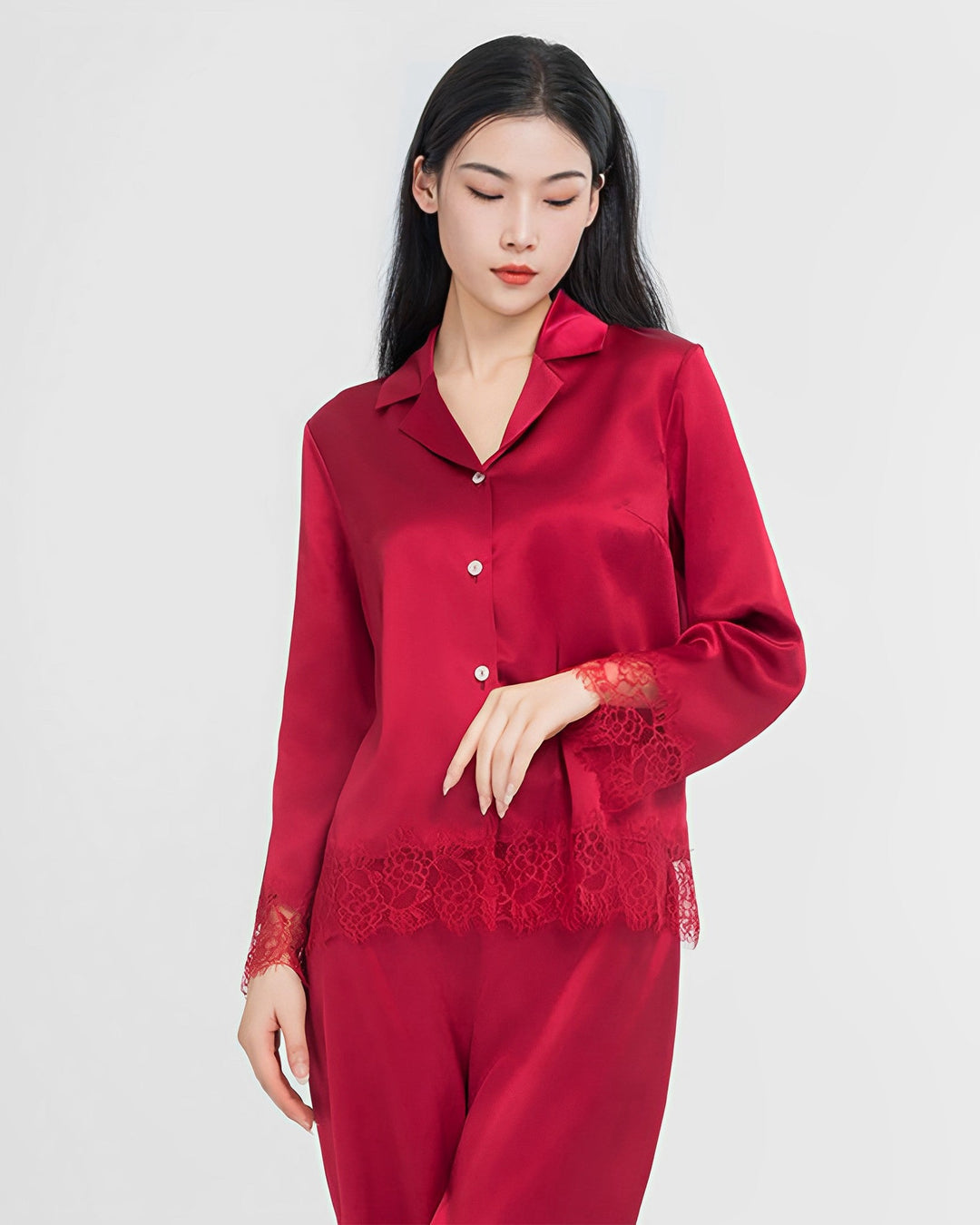 A woman wearing the Premium Lace Silk Pajamas Set from SusanSilk, featuring a red, long-sleeve satin design with lace details on the sleeves and hem, stands against a plain background, showcasing exquisite craftsmanship.