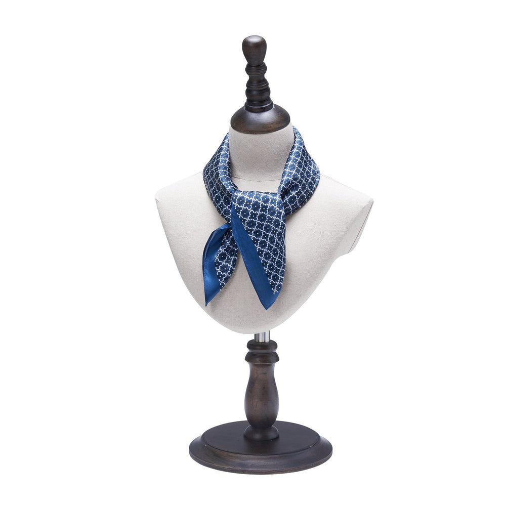 A mannequin bust displays a blue and white patterned Lucky Clover Square Silk Scarf by SusanSilk tied around its neck, set on a wooden stand.