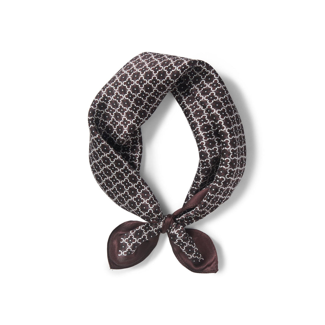 A Lucky Clover Square Silk Scarf by SusanSilk, black and white patterned and tied in a square knot, isolated on a white background.