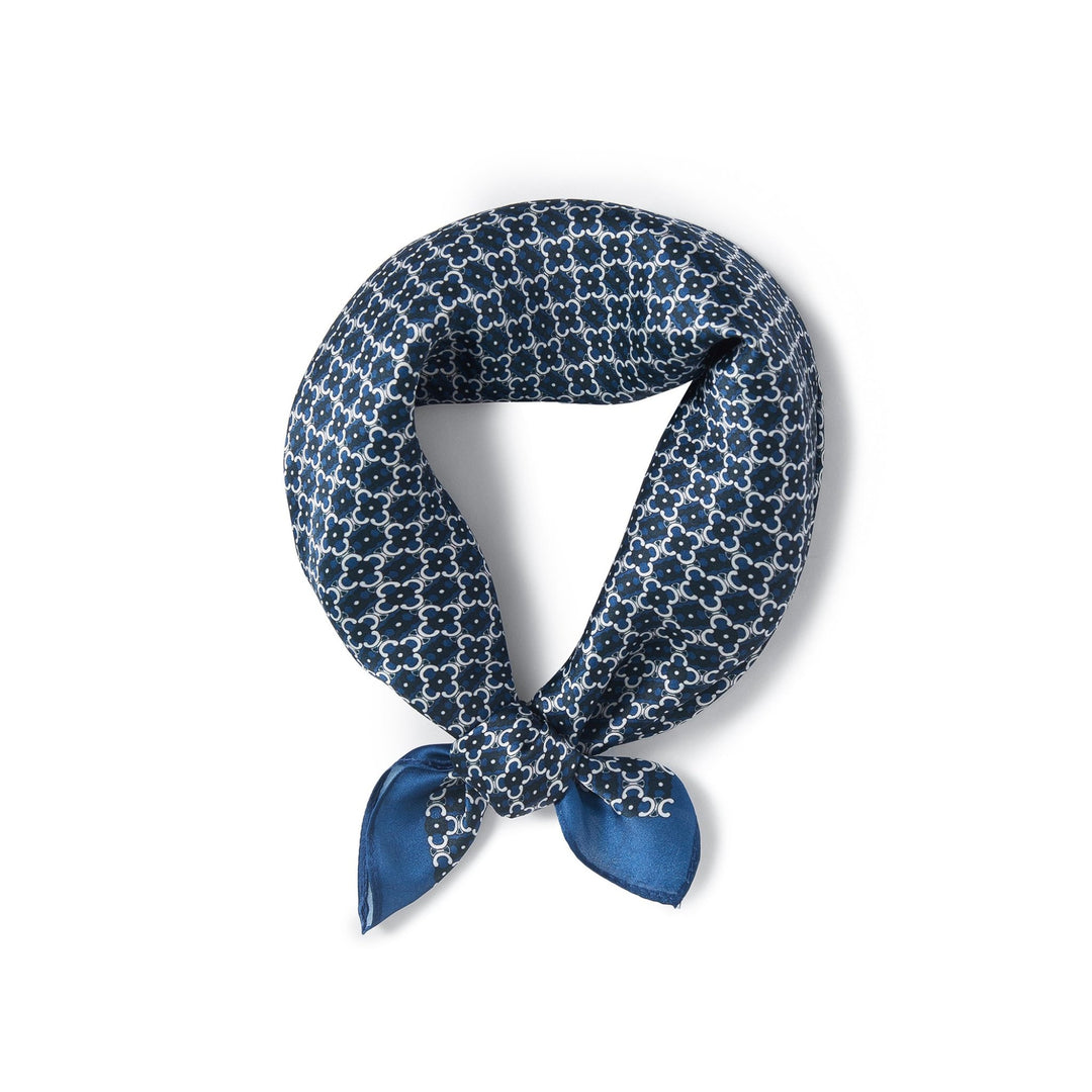 A Lucky Clover Square Silk Scarf from SusanSilk, adorned with a white geometric pattern on blue silk, is neatly tied in a knot to form a loop.